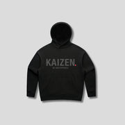 Black hoodie with 'KAIZEN' text, folded flat on grey background